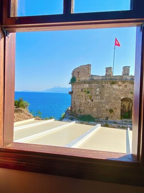 A view through a window of a stone building with a flag, overlooking a body of water and a distant mountain range. - Ulivo Hotel (Antalya)