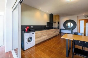 A modern kitchen with a washing machine, a dining area with a table and chairs, and a large mirror on the wall. - Rooms Llançà - Serena Stays (Llançà)
