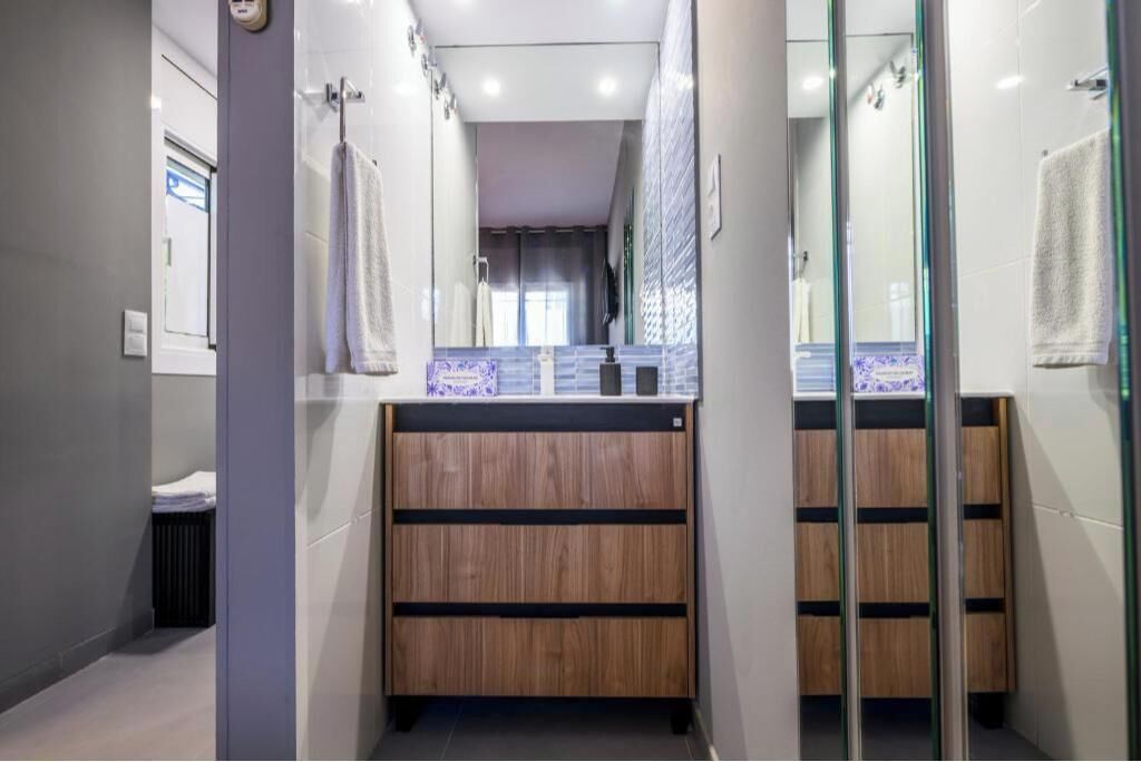 A modern bathroom with a wooden vanity, a glass shower enclosure, and a large mirror.