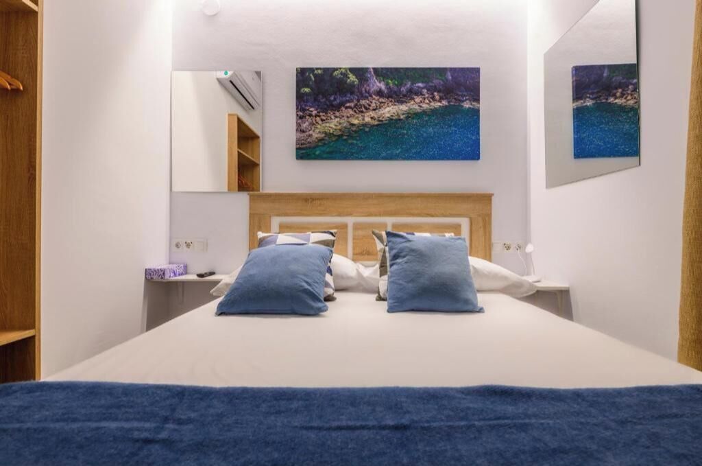 Quarto com cama, duas almofadas, mesa de cabeceira, espelho e duas pinturas penduradas na parede.