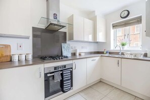 A modern kitchen with a gas stove, oven, and a window with a view of buildings. - Stylish 2BDR House w Parking Near Heathrow (Berkshire)