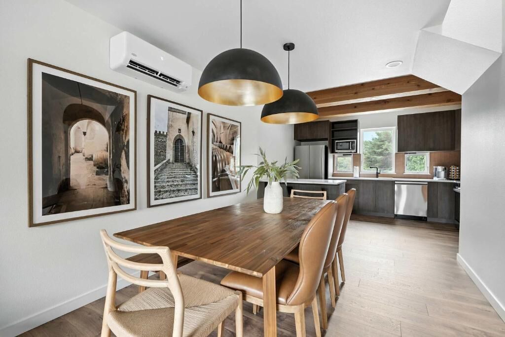 A modern kitchen with a wooden dining table, pendant lights, and framed pictures on the wall.