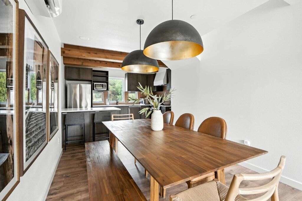 Une cuisine moderne avec une table à manger en bois, des luminaires suspendus et une vue sur l’extérieur.