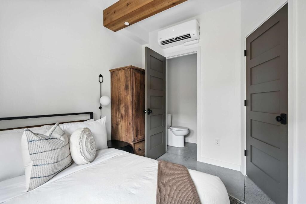 A bedroom with a bed, a wooden wardrobe, a white toilet, and a door.