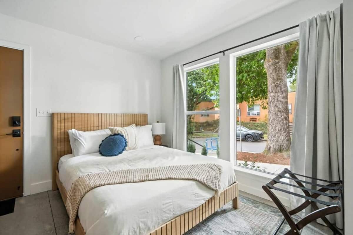 A bedroom with a bed, a window with curtains, and a view of the outside.