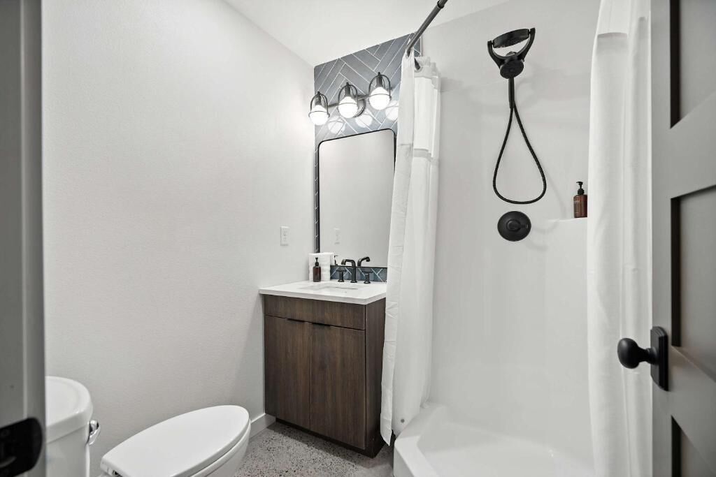 A bathroom with a toilet, sink, mirror, shower, and a door.