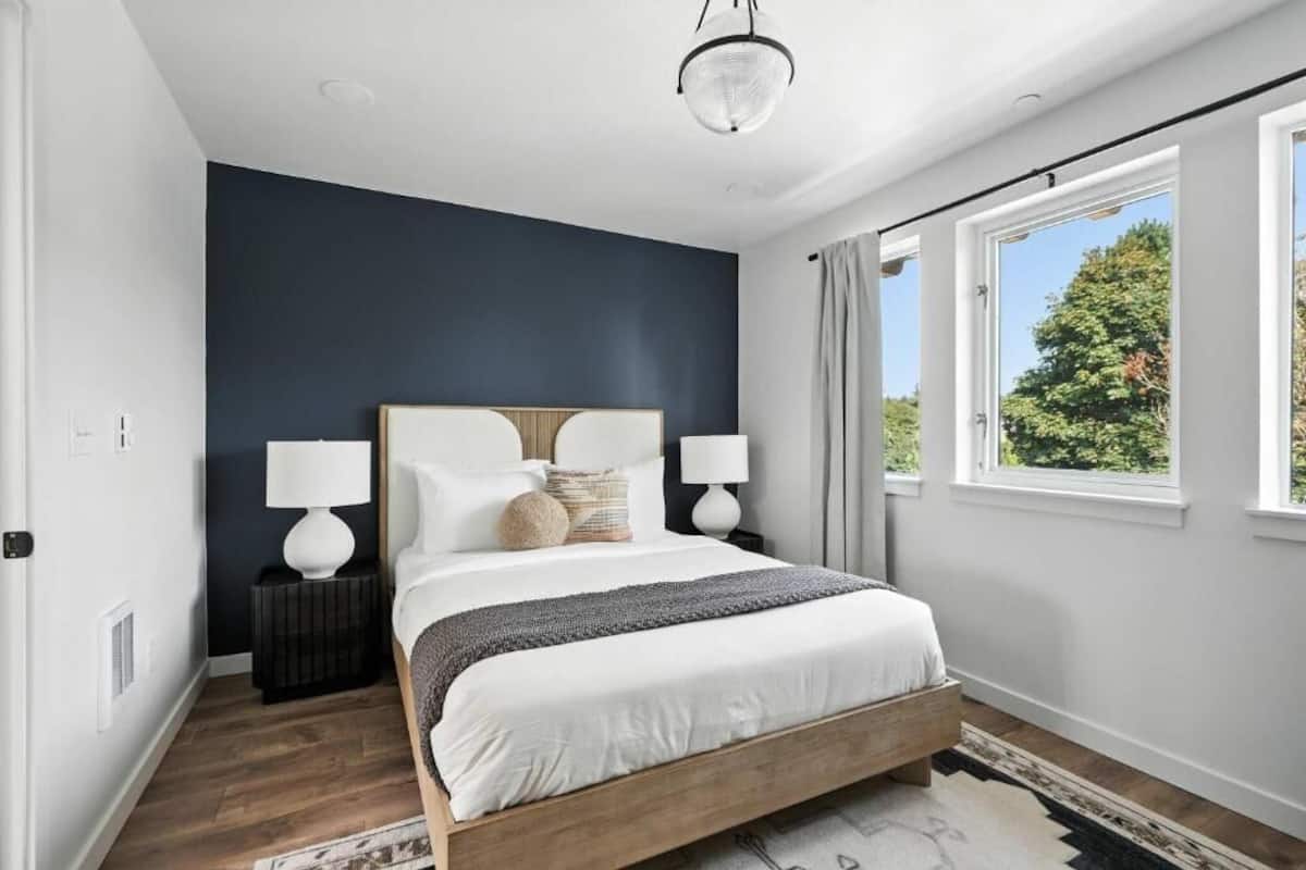 A bedroom with a bed, two bedside lamps, a window, and a view of greenery outside.