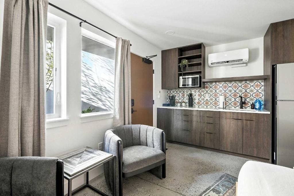 A modern kitchen with a microwave, stove, and cabinets, a dining area with a table and chairs, and a large window with curtains.