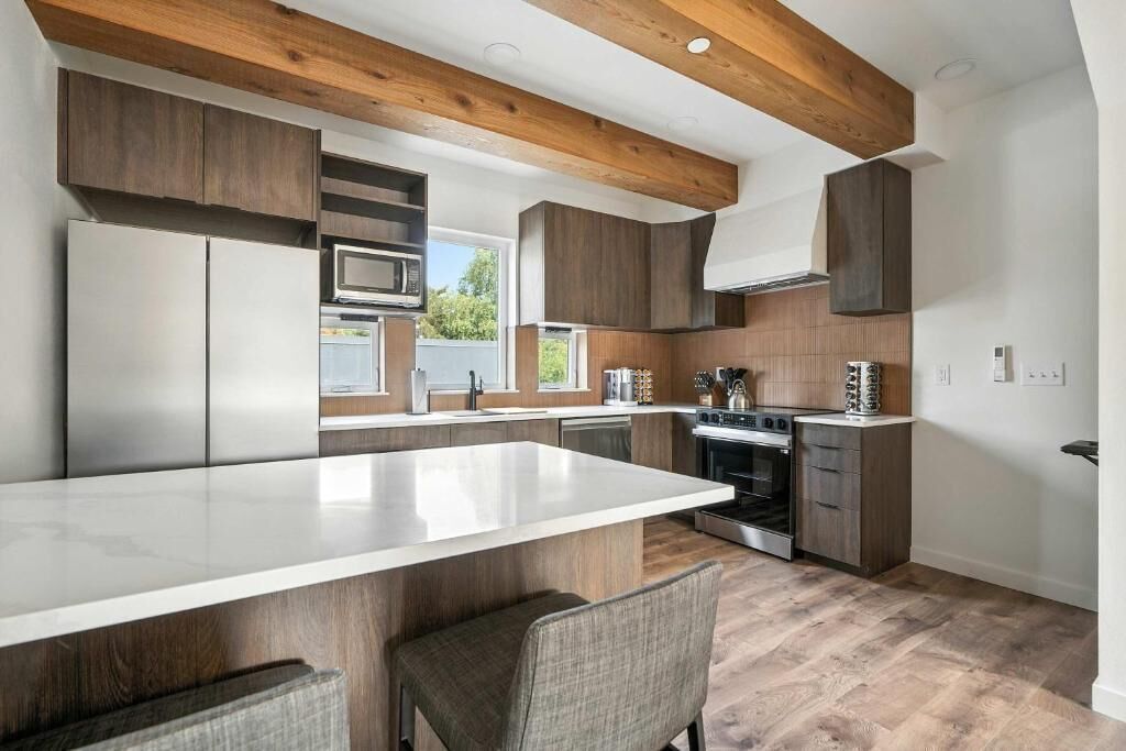 A modern kitchen with a central island, built-in appliances, and wooden beams.