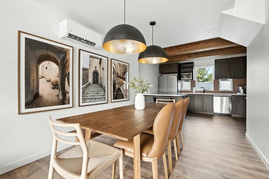 A modern kitchen with a dining area, wooden flooring, pendant lights, and framed pictures on the wall.