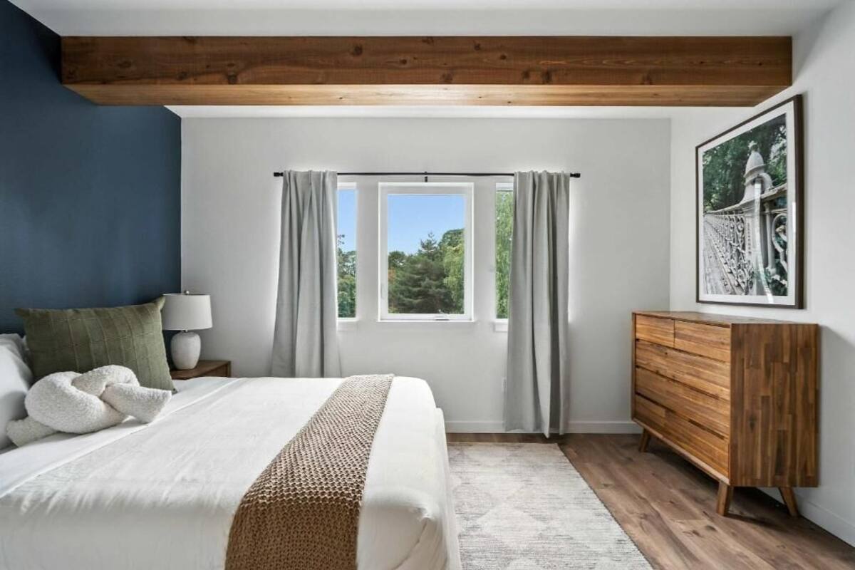 A bedroom with a bed, a wooden dresser, a window with curtains, and a framed picture on the wall.