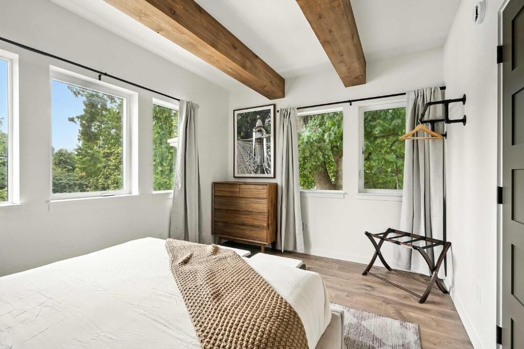 Un dormitorio con cama, cómoda de madera y vistas a árboles a través de amplias ventanas.