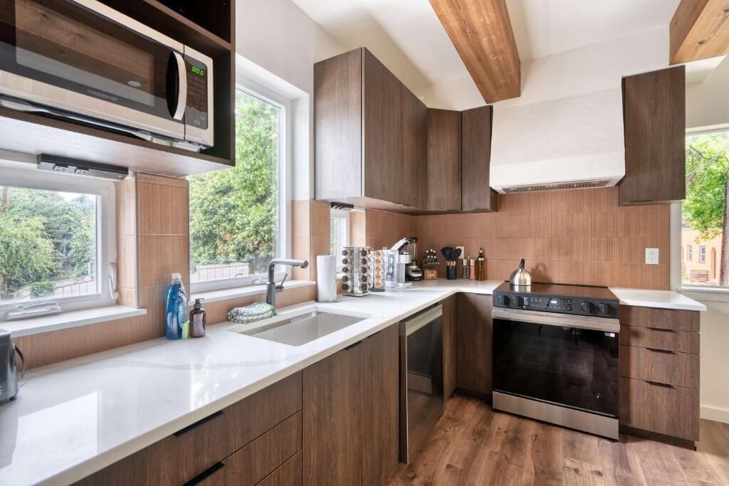 A modern kitchen with wooden cabinets, a built-in microwave, a stainless steel oven, and a large window.