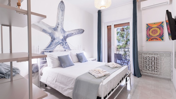 A bedroom with a bed, a large abstract artwork, a hanging light fixture, and a window with a view. - Linda Blue Bay, Sorrento Coast (Piano di Sorrento)