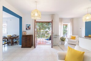 Un vaste espace de vie comprenant une table à manger, un canapé agrémenté d’un coussin jaune et un balcon offrant une vue sur les arbres.