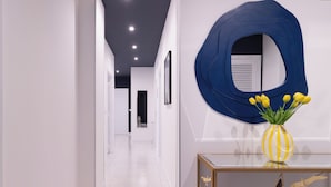 A modern hallway with white walls, a blue abstract wall art piece, and a yellow vase with yellow flowers on a console table. - Linda Blue Bay, Sorrento Coast (Piano di Sorrento)