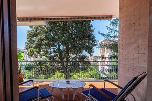 A balcony with a table and chairs, a potted plant, and a view of a tree and buildings. - Linda Blue Bay, Sorrento Coast (Piano di Sorrento)