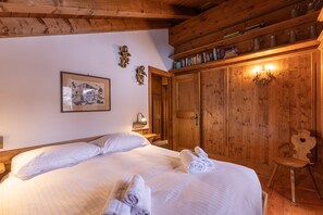 A wooden-paneled room with a bed, a wooden chair, a shelf with books, and a wall-mounted picture. - Casa Punta Nera 2, spacious and comfortable (Cortina d´Ampezzo)
