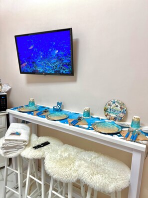 Une pièce avec un téléviseur diffusant des images du monde sous-marin, une longue table dressée avec des assiettes, des couverts et un panneau décoratif accueillant les visiteurs.