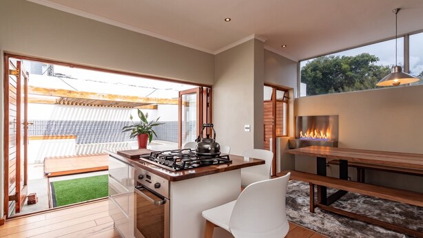 A modern kitchen with a gas stove, white chairs, and a dining table. - 3-bedroom house with mountain views, pool and fireplaces in Cape Town. (Cape Town)