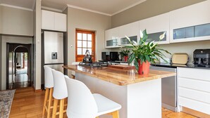 A modern kitchen with a central island, white bar stools, stainless steel appliances, and a potted plant. - 3-bedroom house with mountain views, pool and fireplaces in Cape Town. (Cape Town)