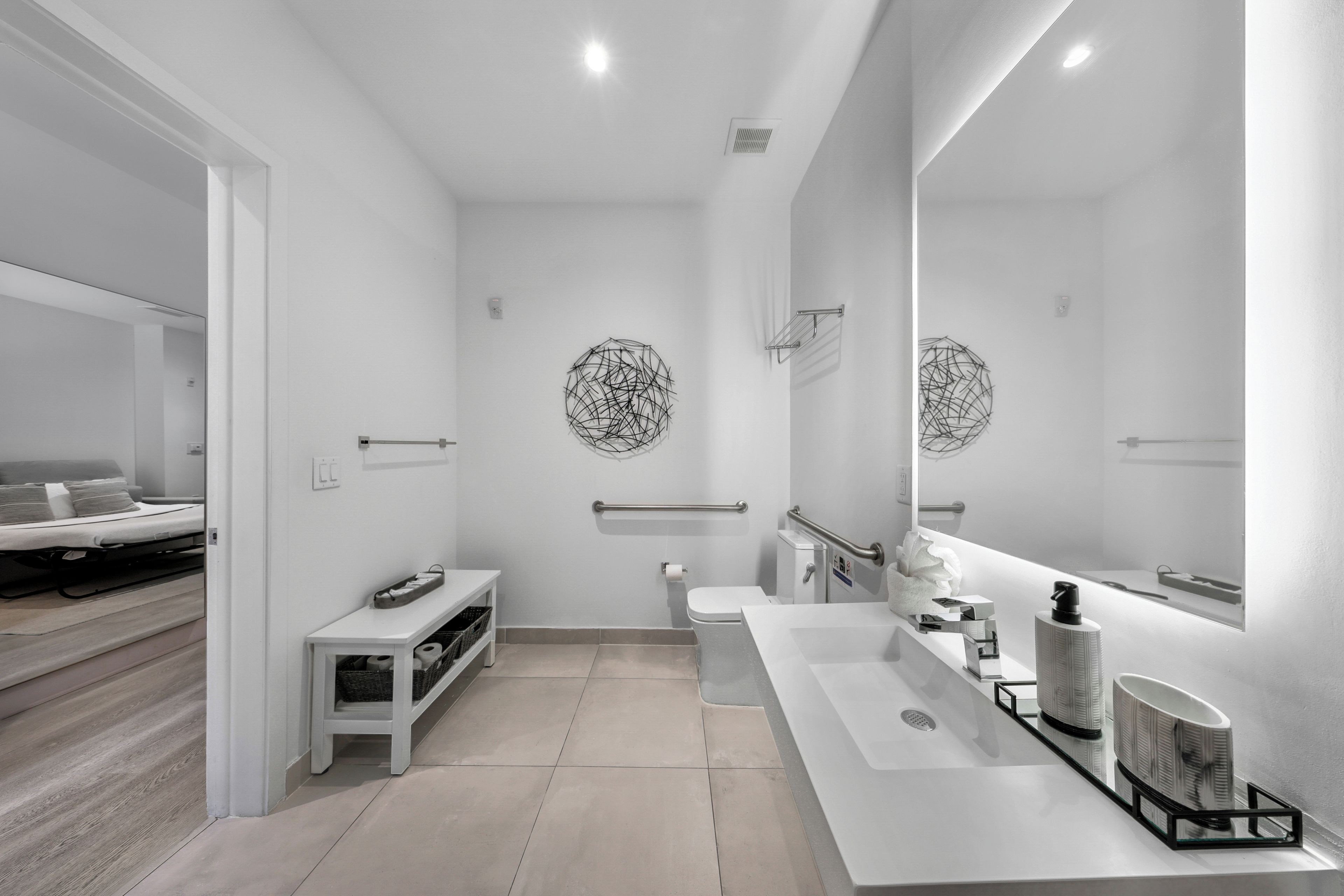 Un baño moderno con un espejo grande, un inodoro, un lavabo y un banco.