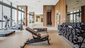 A gym with exercise equipment, weight racks, and large windows. - Brickell Building City Centre - We Host (Miami)