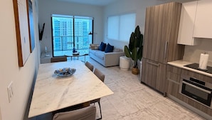 A modern kitchen with a dining area, a large window, and a view of high-rise buildings. - Brickell Building City Centre - We Host (Miami)