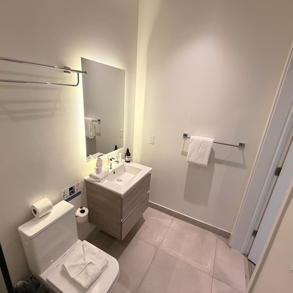 Un baño moderno con inodoro, lavamanos, espejo y toallero.