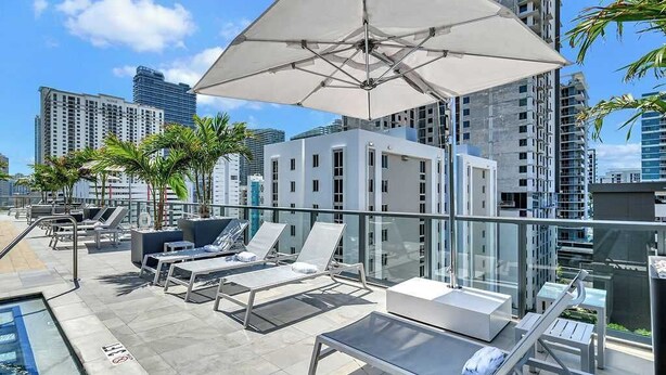A rooftop lounge with sun loungers, a pool, and a glass balustrade overlooking a cityscape. - Brickell Building City Centre - We Host (Miami)