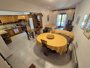 A spacious living area with a dining table, sofas, and a kitchen in the background.