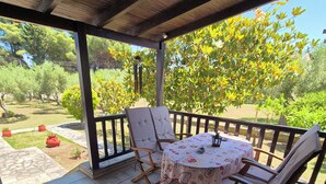 Eine überdachte Terrasse mit Tisch und Stühlen, Blick auf einen Garten mit Bäumen und einer Rasenfläche.