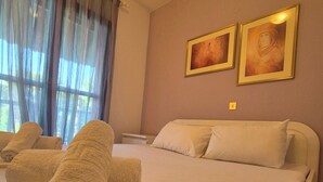 Ein ordentlich bezogenes Bett mit aufgerollten Handtüchern, einem Nachttisch und zwei gerahmten Kunstwerken an der Wand.