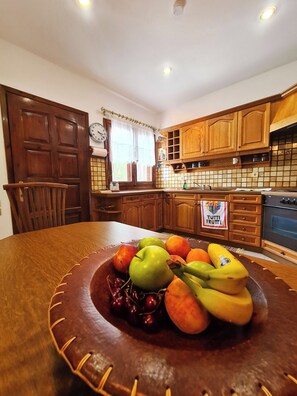 A kitchen with wooden cabinets, a clock, and a fruit bowl on the table.