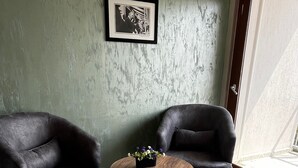 Una habitación con dos sillones, una mesa de centro redonda de madera, baldosas de suelo con diseños, un cuadro en la pared y un ventanal grande.