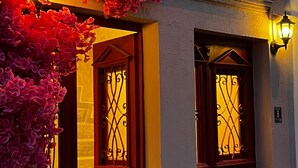 Entrada de un edificio con dos puertas rojas, una reja de hierro forjado y una planta en maceta.