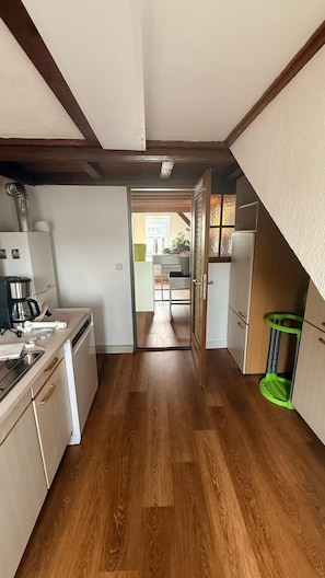 Eine schmale Küche mit Holzboden, einer Kaffeemaschine und einem Kühlschrank.