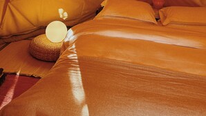 Ein gemütlicher, zeltartiger Raum mit einem Bett, Kissen und einem gewebten Korb. An der Wand ist ein dekorativer Gegenstand mit einem Flügeldesign zu sehen.