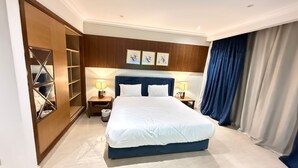A hotel room with a large bed, two bedside tables with lamps, a wooden wardrobe, and a large window with curtains. - Apartment beside Airport, City stars Nasr City with AC (Cairo Governorate)