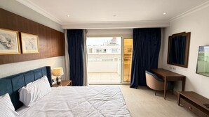 A hotel room with a bed, a desk, a chair, a lamp, a TV, and a view of the city through the window. - Apartment beside Airport, City stars Nasr City with AC (Cairo Governorate)