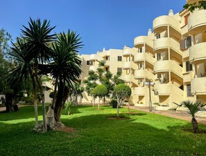 Edifício residencial com várias varandas e um jardim bem cuidado com palmeiras.