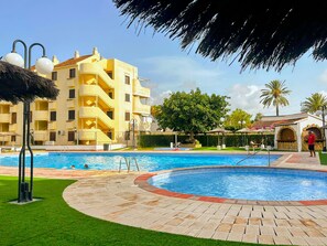 Piscina cercada por um espaço pavimentado, com um edifício ao fundo.