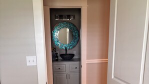 A hallway with a wooden floor, a white door, and a bathroom with a round mirror and a sink. - South Alabama Country Home With A Swimming Pool (Fairhope)