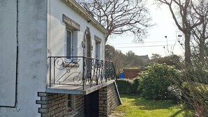A building with a stone base and a white upper section, featuring a balcony with a metal railing and a stone archway. - Renovated country house close to the ocean and hiking trails. (Névez)