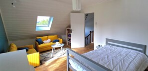 Ein Zimmer mit einem Bett, einem Schlafsofa, einem kleinen Tisch, einem Bücherregal und einem Oberlicht.