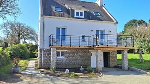A two-story house with a stone facade, a balcony with a black railing, and a small garden area. - Renovated country house close to the ocean and hiking trails. (Névez)