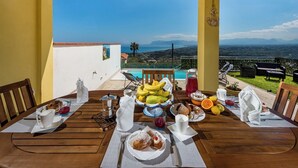Ein Frühstückstisch mit Blick auf Pool und Berge, mit Bananen, Brot und einer Obstschale.