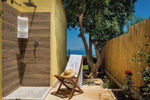 Un espace détente avec une douche en bois, une serviette posée sur une chaise et une vue sur la mer.