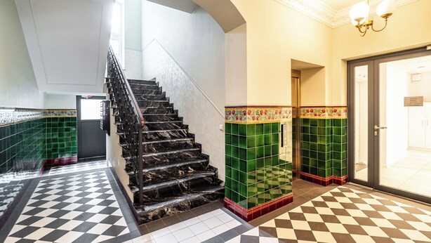 Un escalier avec des marches en marbre noir, des murs recouverts de carreaux verts et un motif de sol à carreaux.