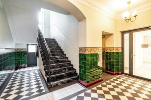 A staircase with black marble steps, green tiled walls, and a checkered floor pattern. - RentPlanet - Apartament Chopina (Katowice)